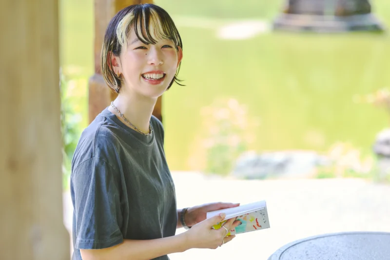 本を開き笑顔のひらいめぐみさん